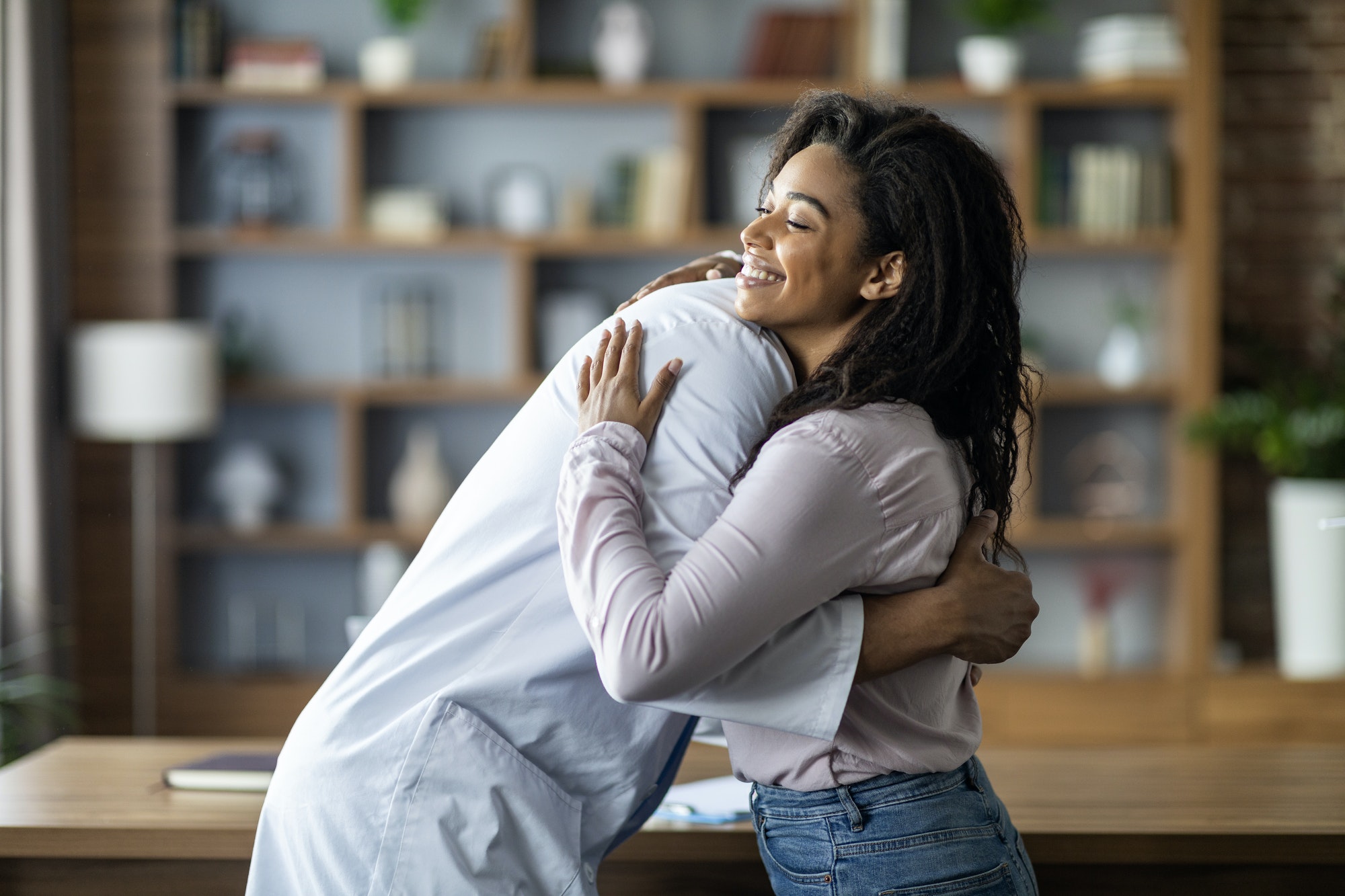 Doctor hugging cheerful black lady patient, clinic interior